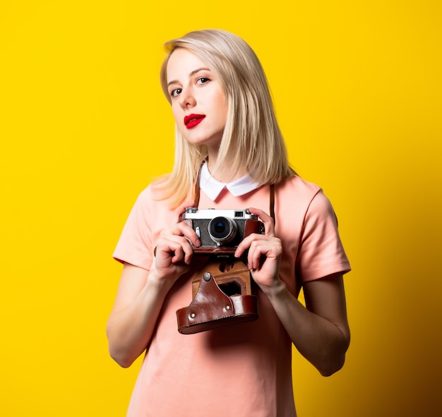 Blond meisje in roze jurk met vintage camera op gele ruimte