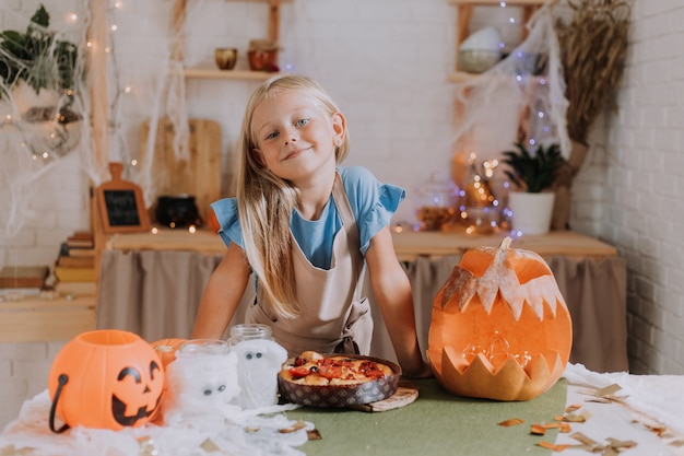 Blond meisje in schort in de keuken versierd met pompoenen voor halloween bereidt een focaccia-taart