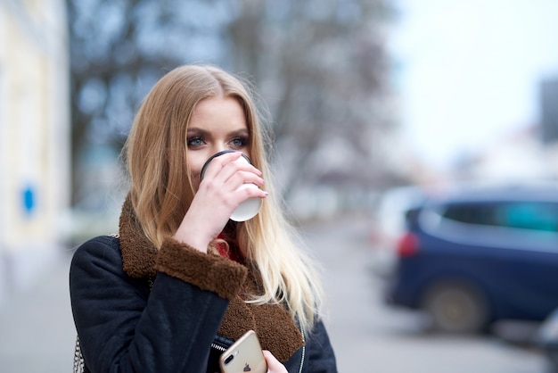 Blond meisje loopt door de stad en drinkt koffie