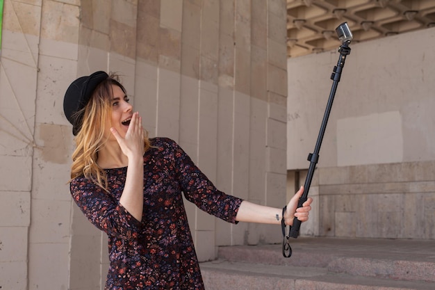 Blond meisje maakt selfie met een selfiestick en sluit haar mond met een hand