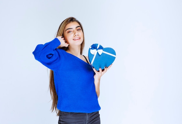 Blond meisje met een blauwe geschenkdoos in de vorm van een hart.