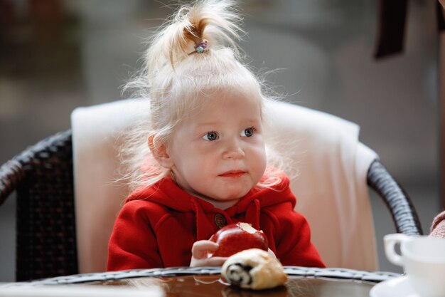 Blond meisje met een staart eet een appel aan een tafel in een café.