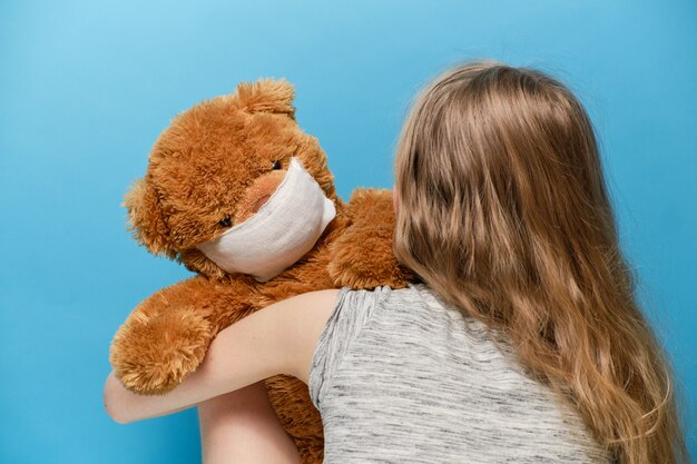 blond meisje met een teddybeer in een masker in haar armen. pandemie quarantaine concept