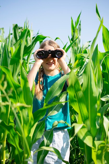 Foto blond meisje met een verrekijker in de groene korenveld zomer