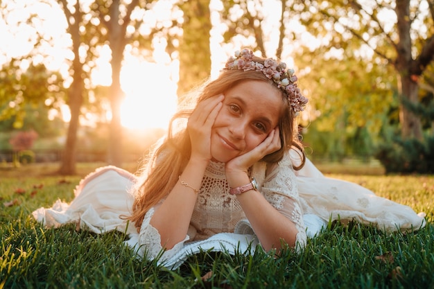 Foto blond meisje met krullend haar gekleed in communie jurk liggend op het gras voor foto's