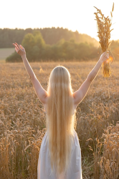 Foto blond meisje met lang haar met opgeheven handen in een tarweveld bij zonsondergang soft focus