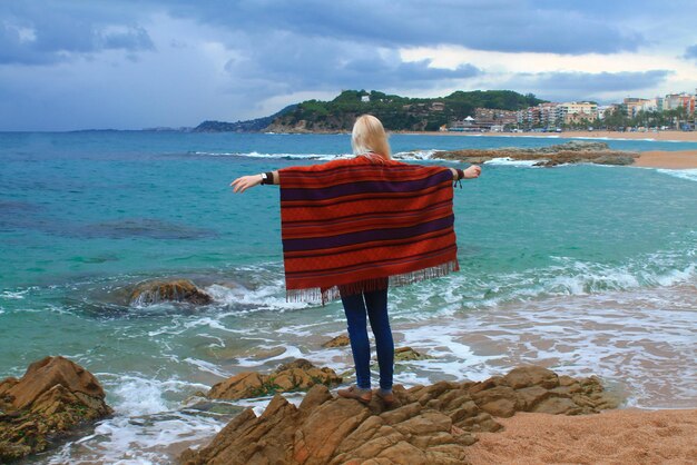 Blond meisje op een rots in een poncho. de kust van lloret de mar. catalonië. spanje.