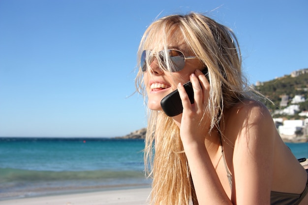 Blond meisje op mobiele telefoon op het strand