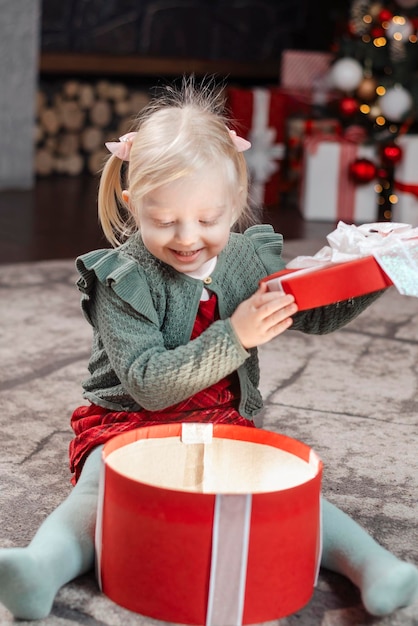 Blond meisje opent kerstcadeaus Gewenst cadeau Verbaasd klein kind dat kerstcadeau opent