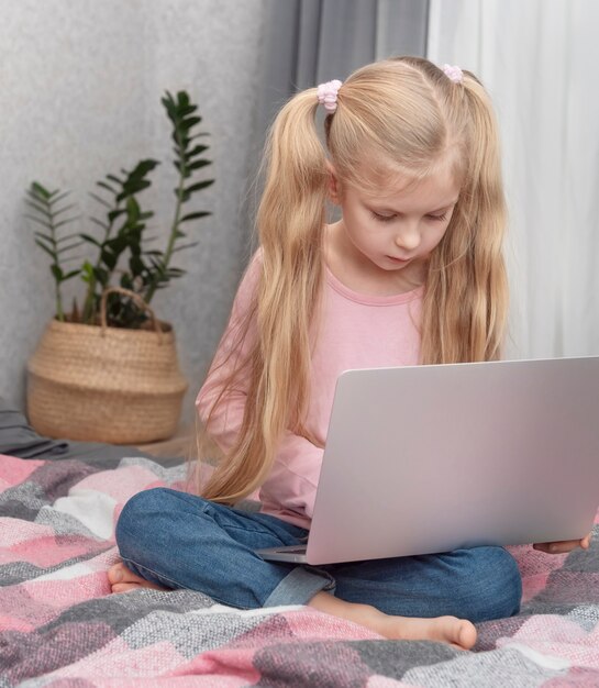 Blond meisje studeert thuis online met een laptop in bed