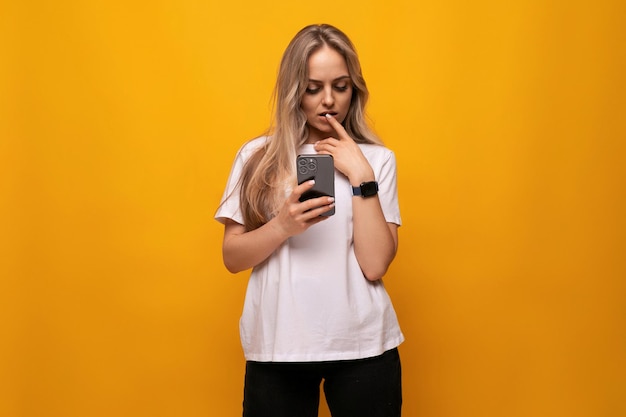 Blond meisje telt in gedachten kijkend naar het smartphonescherm op een oranje achtergrond