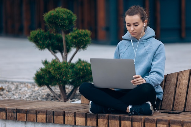 Blond meisje zittend op een bankje in het park met laptop