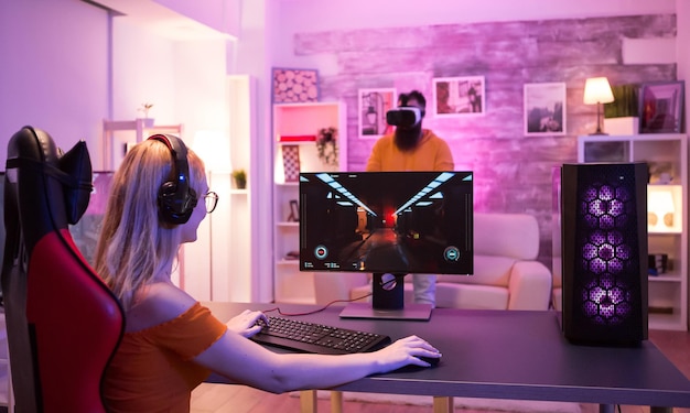 Blond meisje zittend op een gamestoel in een kamer met kleurrijk neonlicht. man die games speelt met een vr-bril.