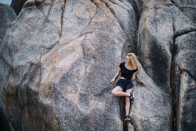 blond meisje, zittend op een rotsformatie aan het strand in Thailand