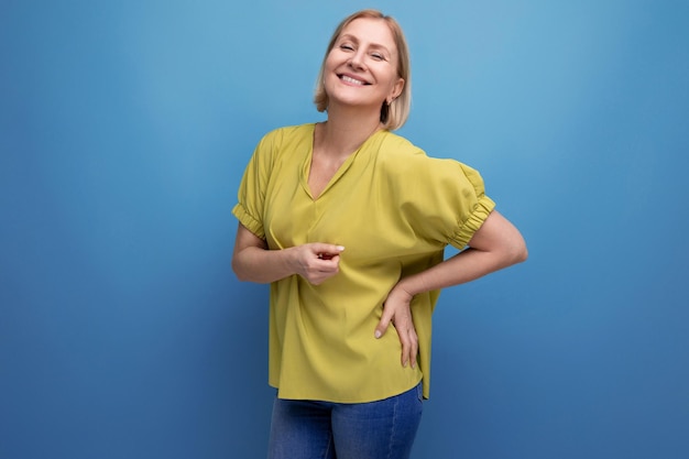 Blond middle aged woman showing cheerful emotions on studio background with copy space