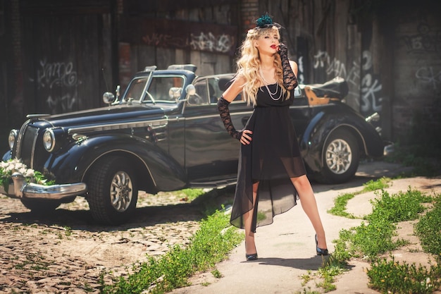 Foto blond model poseren in de buurt van retrostyled zwarte auto buitenshuis