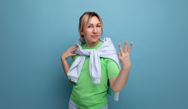 Blond positive bright girl in a casual outfit shows three fingers on a blue background with copy