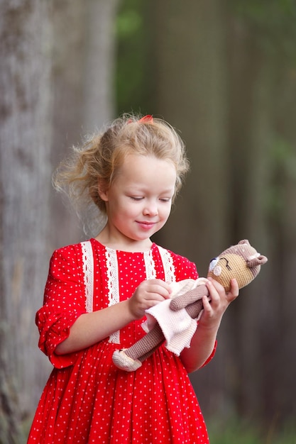 a blond preschool girl in a wreath of rowan and with toys walks in the park on a summer morning