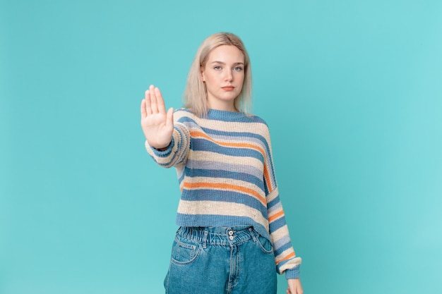 Blond pretty woman looking serious showing open palm making stop gesture