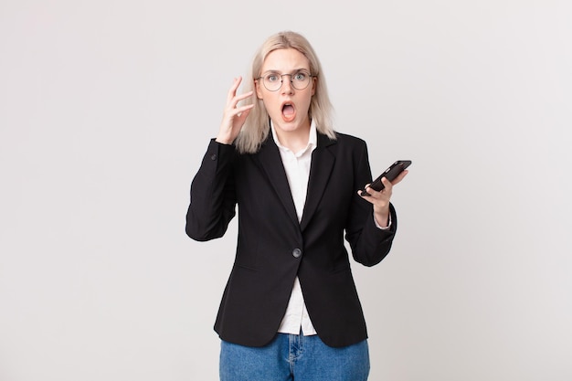 Blond pretty woman screaming with hands up in the air and holding a mobile telephone