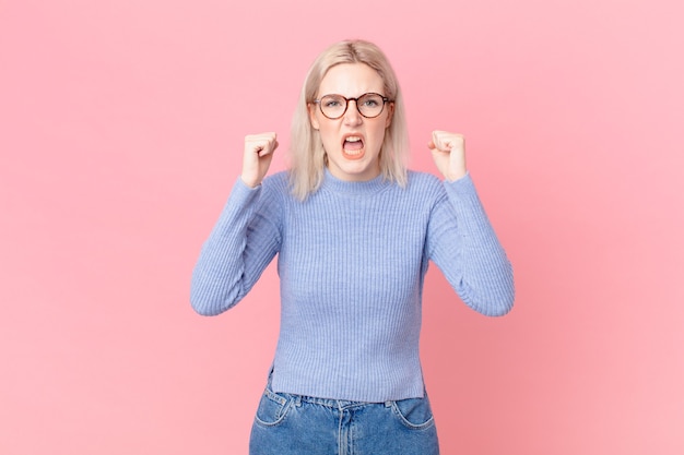 Blond pretty woman shouting aggressively with an angry expression