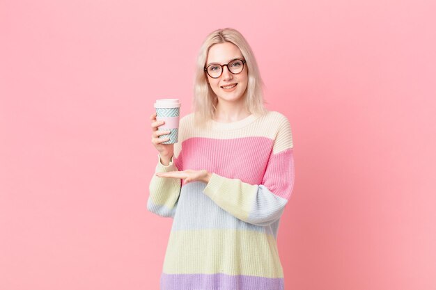 Donna graziosa bionda che sorride allegramente sentendosi felice e mostrando un concetto di caffè di concetto