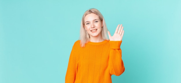 Bella donna bionda che sorride felice, agitando la mano, accogliendoti e salutandoti