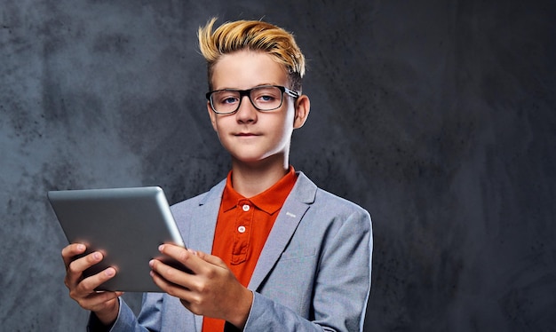 Blond schooler boy in eyeglasses holds tablet PC.