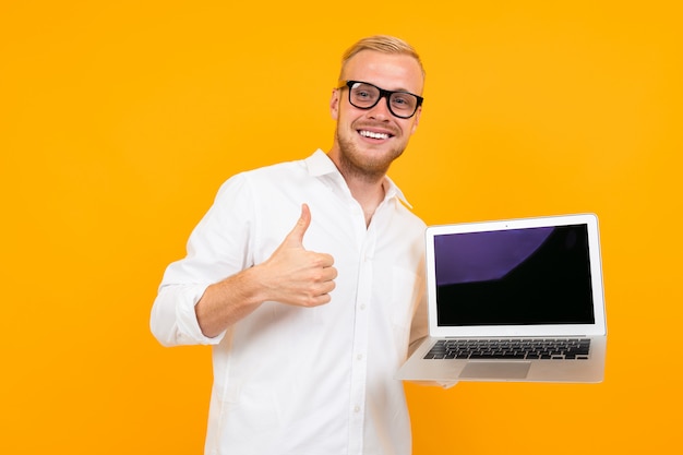 Blond smart smiling businessman in white shirt with laptop wall on yellow wall