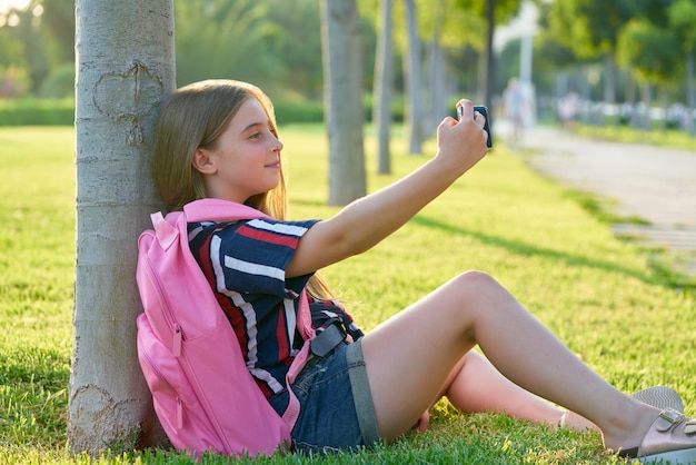 公園でスマートフォンを持つ金髪の学生子供女の子