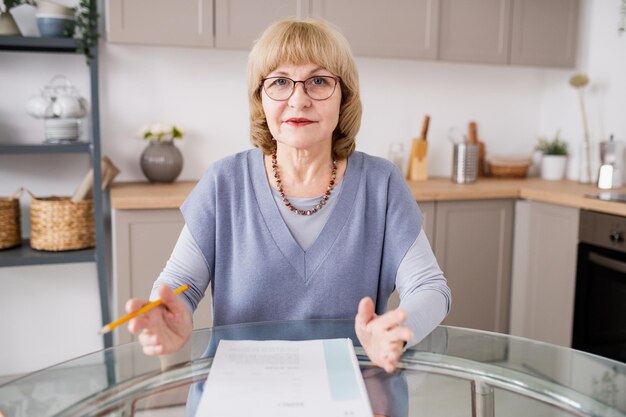 Blond teacher in casualwear and eyeglasses explaining something to online audience