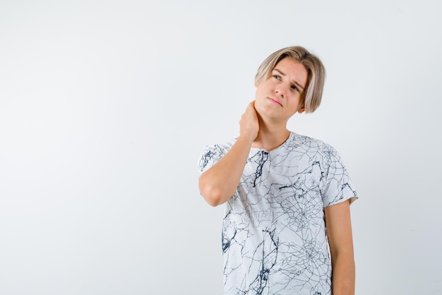 The blond teenager guy is thinking by holding his hand behind his neck on white background