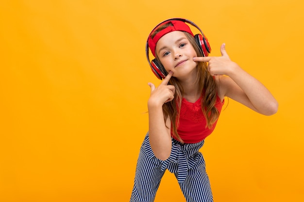 Blond tienermeisje luistert naar muziek in grote koptelefoon op een abonnement in een afspeellijsttelefoon op een gele achtergrond.