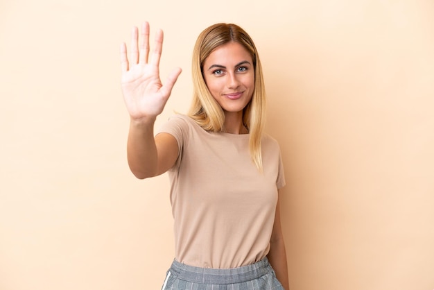 Blond Uruguayaans meisje geïsoleerd op beige achtergrond telt vijf met vingers