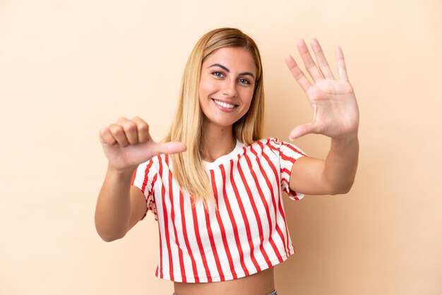 Blond Uruguayaans meisje geïsoleerd op beige achtergrond telt zes met vingers