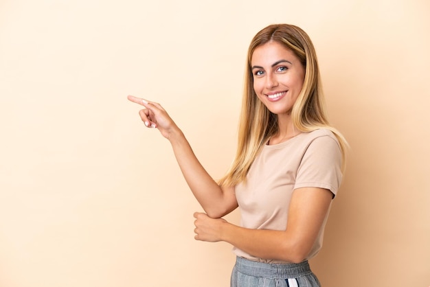 Blond Uruguayaans meisje geïsoleerd op beige achtergrond wijzende vinger naar de zijkant