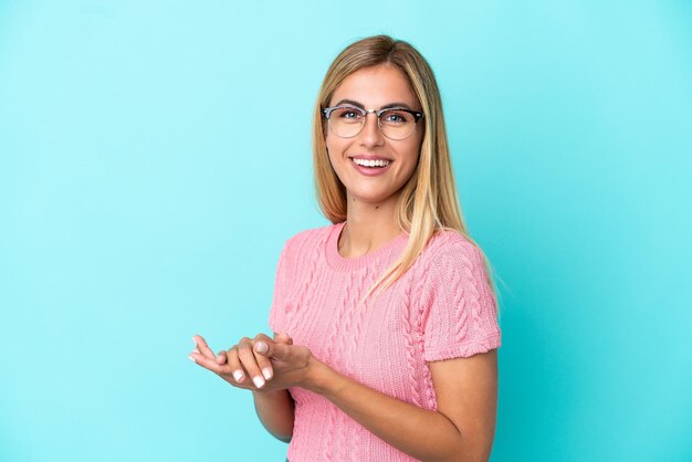 Blond Uruguayaans meisje geïsoleerd op blauwe achtergrond applaudisseren