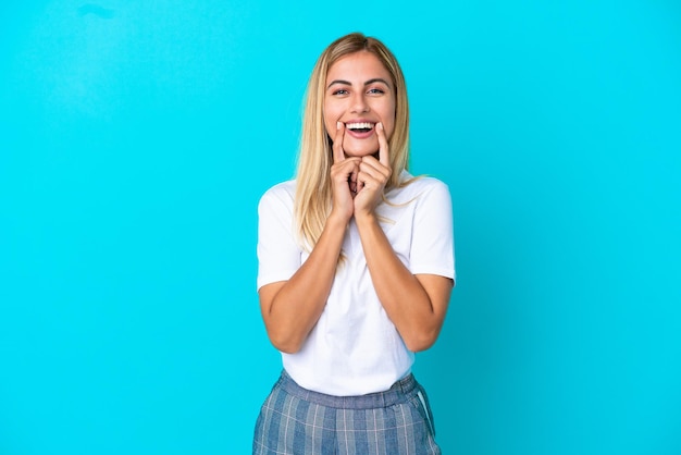 Blond Uruguayaans meisje geïsoleerd op blauwe achtergrond glimlachend met een gelukkige en aangename uitdrukking