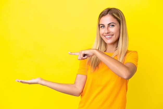 Blond Uruguayaans meisje geïsoleerd op gele achtergrond met copyspace denkbeeldig op de palm om een advertentie in te voegen