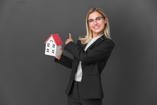 Foto blond uruguayaans meisje met een huisspeelgoed geïsoleerd op een zwarte achtergrond die naar achteren wijst