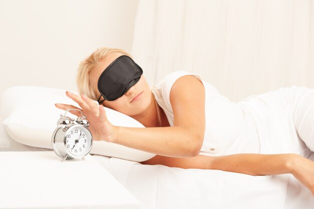 Blond woman in bed looking annoyed at her alarm clock in the morning