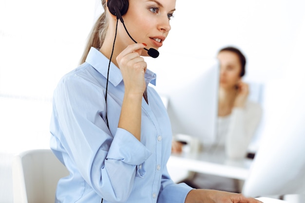 Blond woman call operator is using computer and headset for consulting clients online Group of diverse people working as customer service occupation Business concept