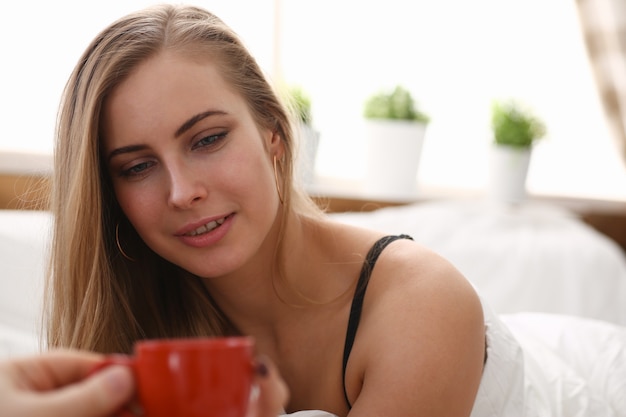 Blond woman have cup of tea coffee early morning in her bed