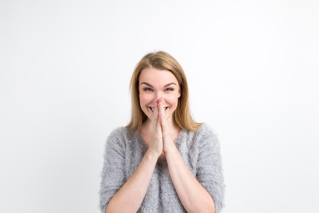 Blond woman is really happy. She is smiling widely with her palms near her face and looking at the viewer. Concept of joy. Mock up