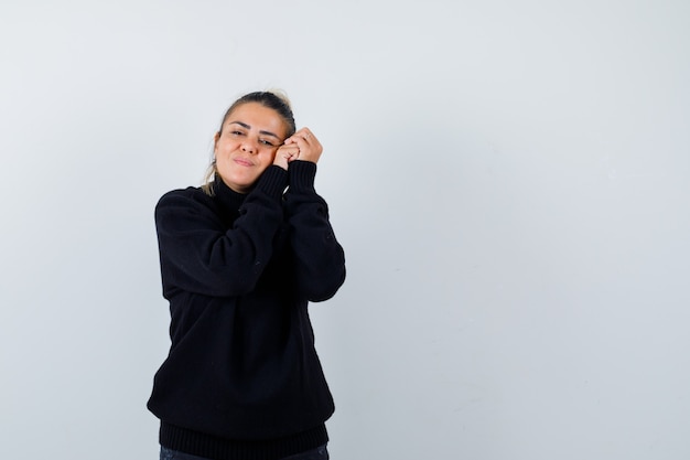 Blond woman leaning head on hands in black sweater and looking dreamy , front view.