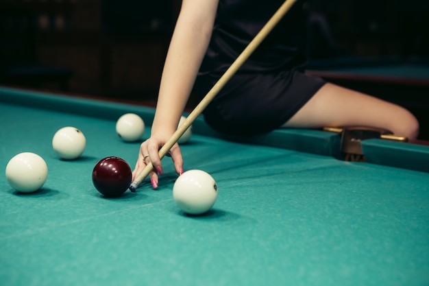 Blond woman playing enjoying billiard hold cue hit white billiard balls on table with green surface