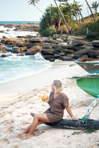 Blond Woman Sit on Beach Drink Coconut Juice