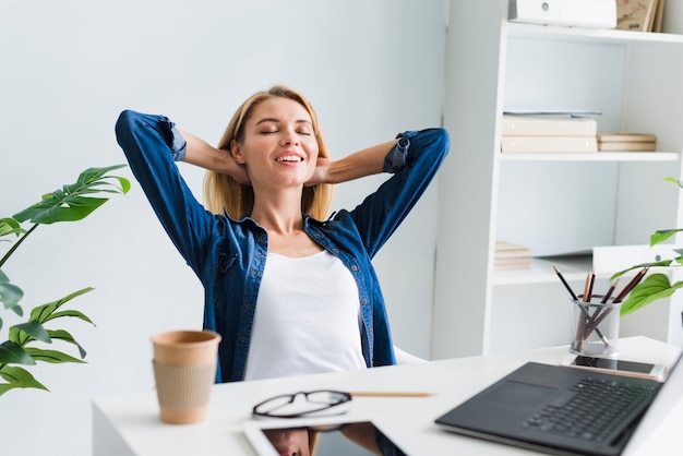 Photo blond woman sitting back and smiling with closed eyes at workplace