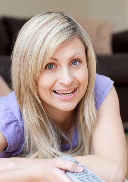 Photo blond woman watching tv lying on the floor