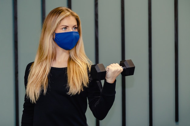 Foto donna bionda che indossa la maschera facciale formazione in palestra durante la pandemia.